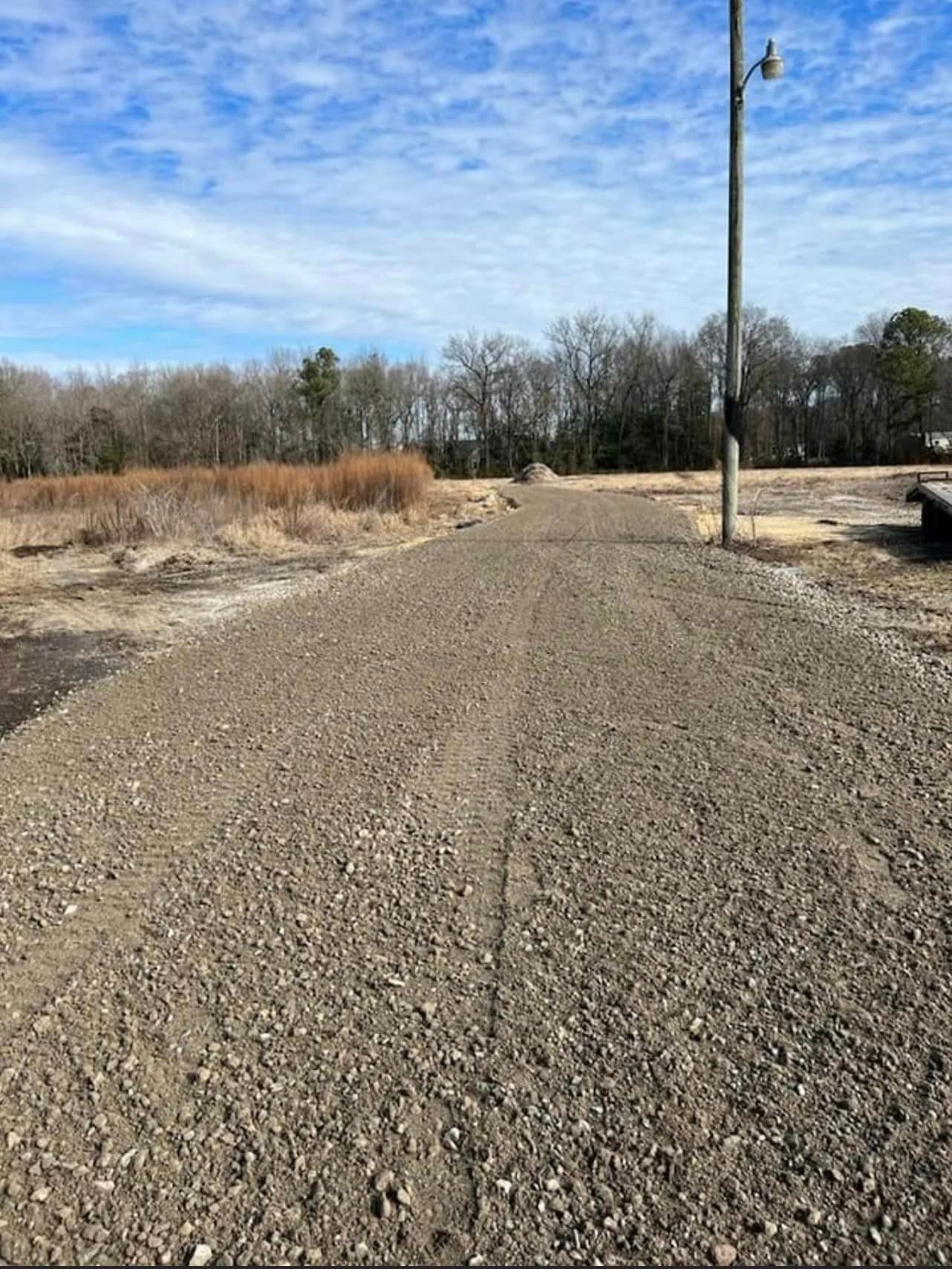 A gravel road going through a field with trees in the background.