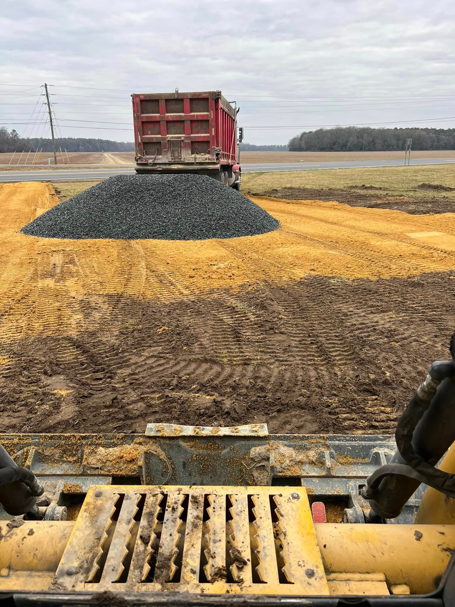 A bulldozer is moving dirt in a field with a dump truck in the background.