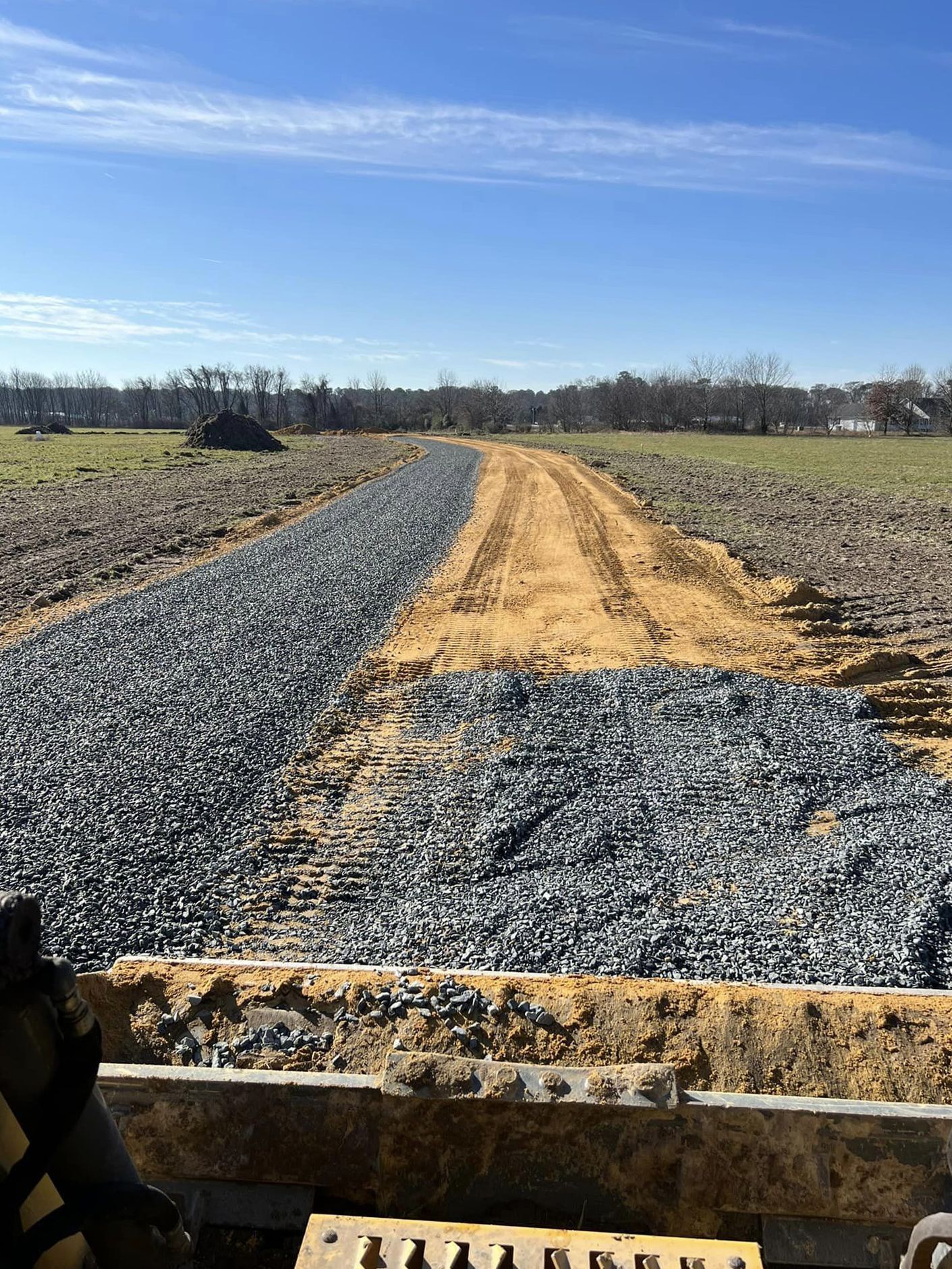 A bulldozer is moving gravel on a dirt road in a field.