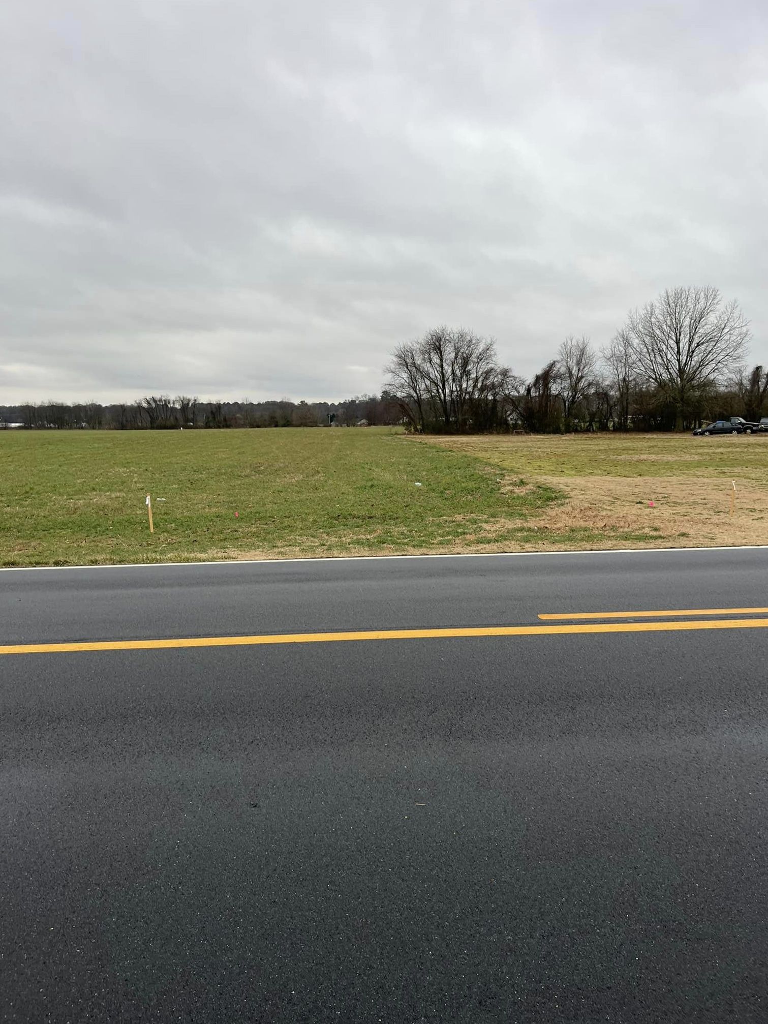 A road with a field in the background on a cloudy day.