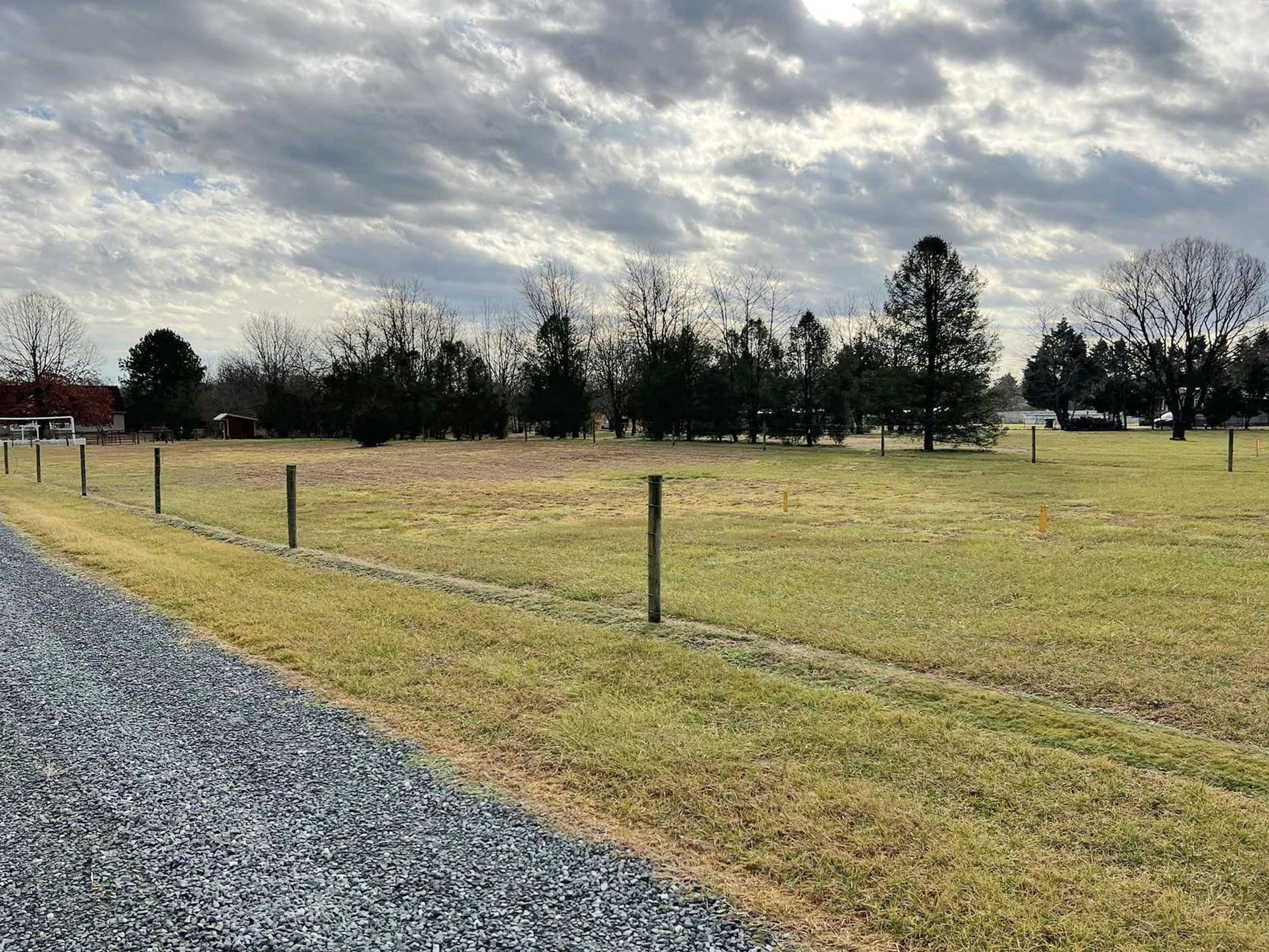 A gravel road going through a grassy field with trees in the background.