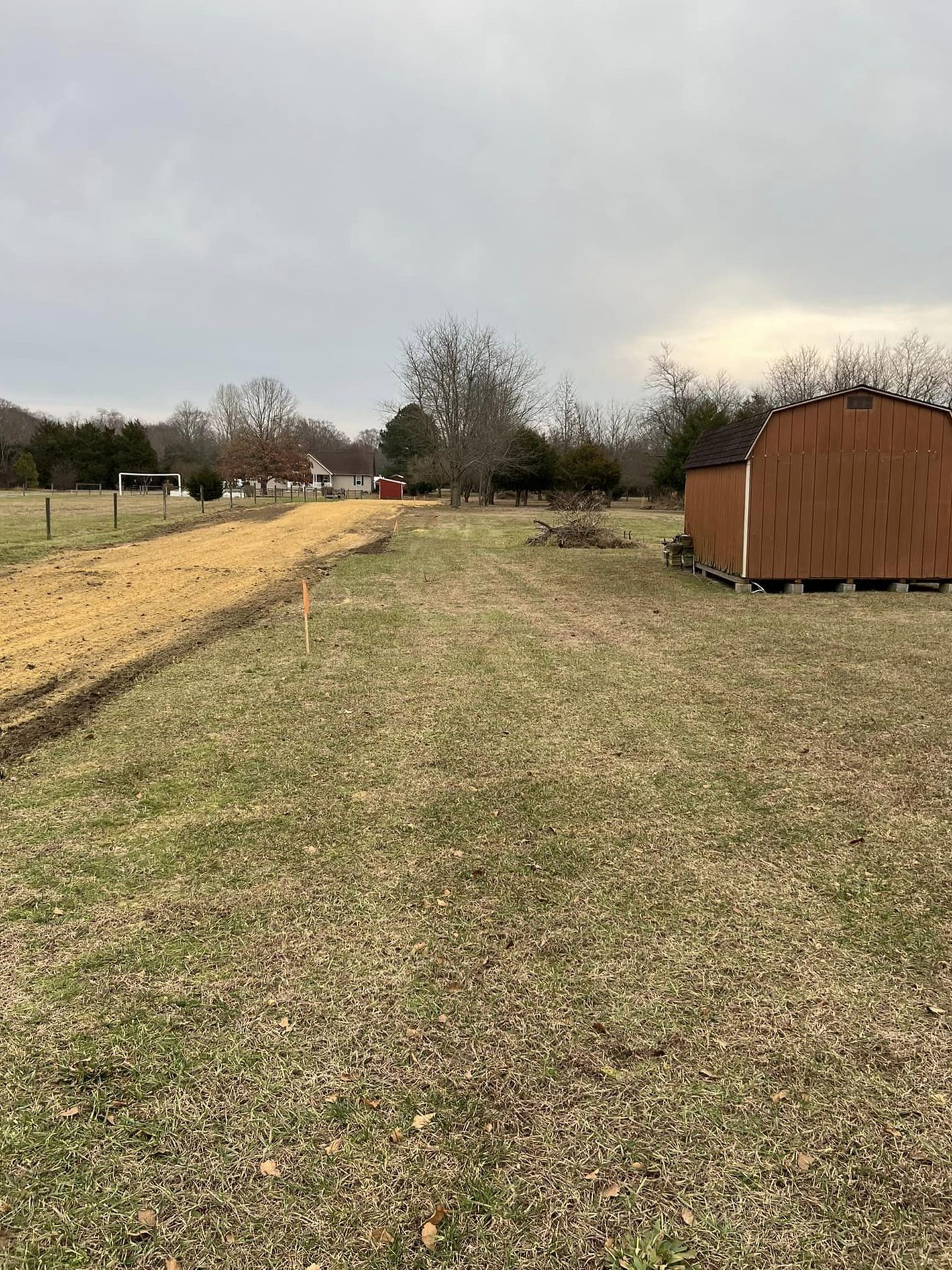 A dirt road going through a grassy field with a shed in the background.