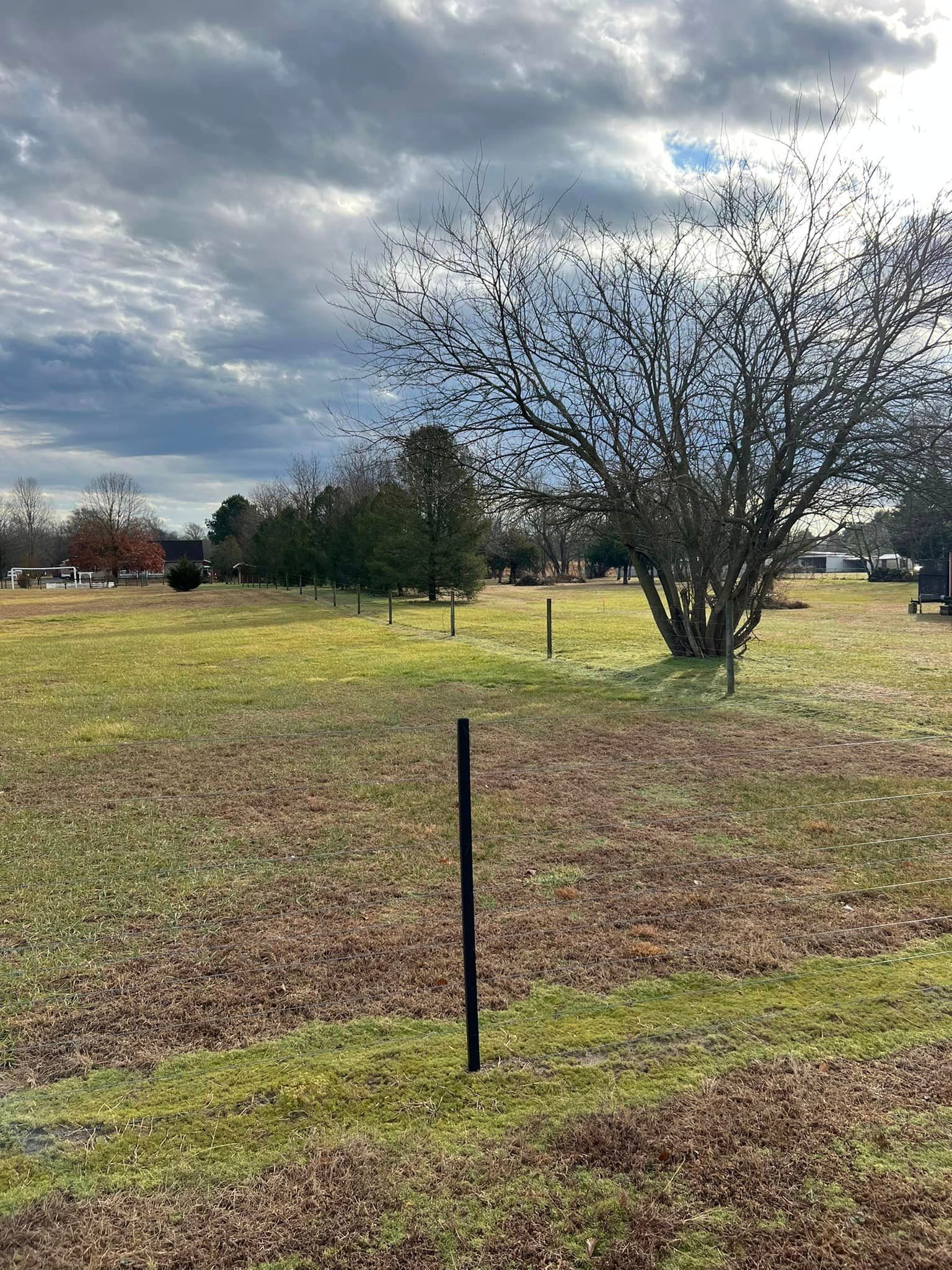 There is a fence in the middle of a field with trees in the background.