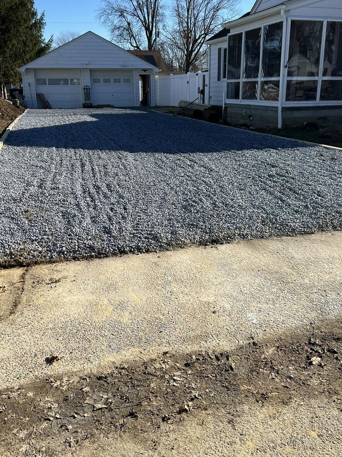 A gravel driveway leading to a house with a screened in porch.
