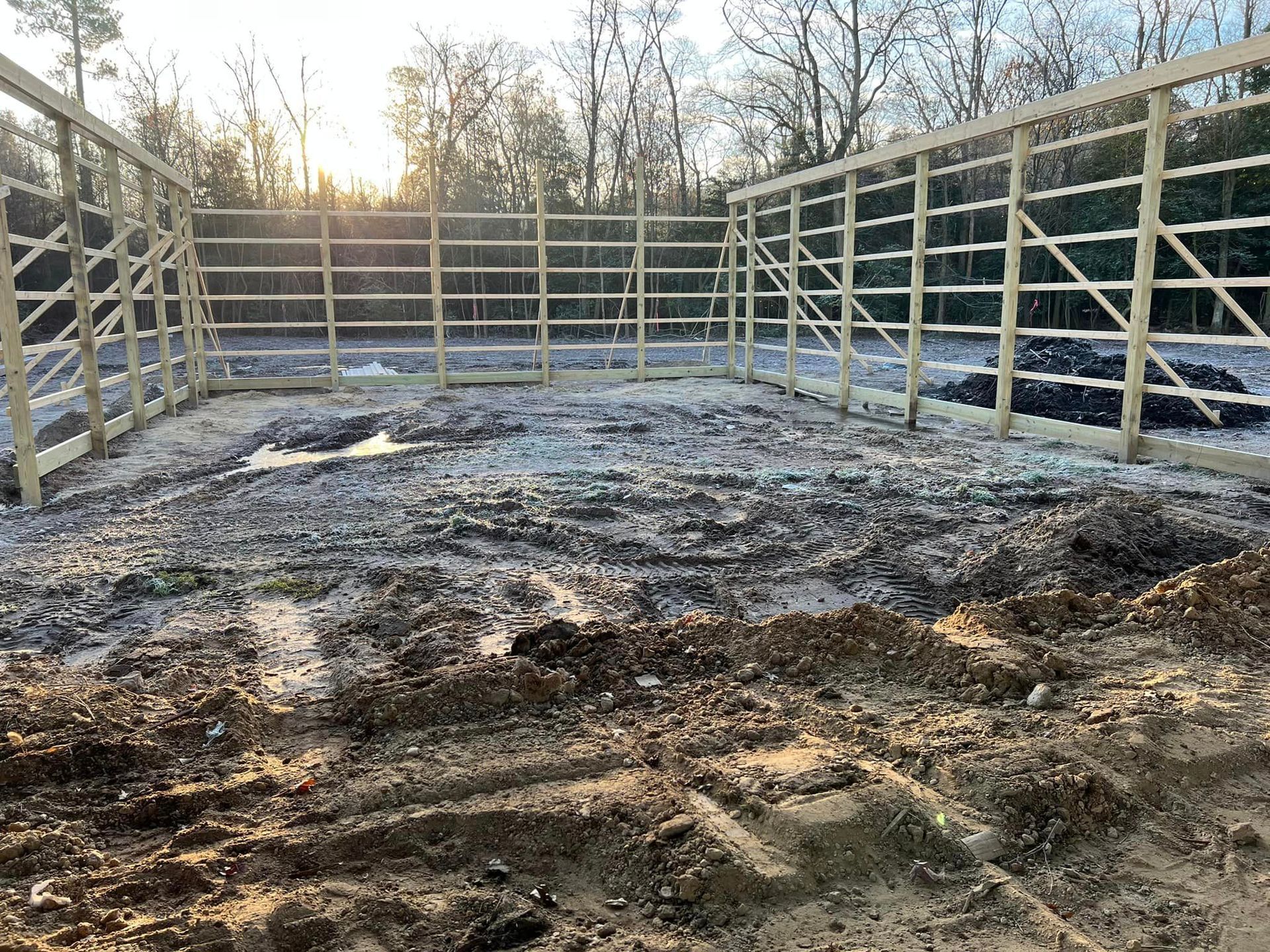 A muddy field with a fence and trees in the background.