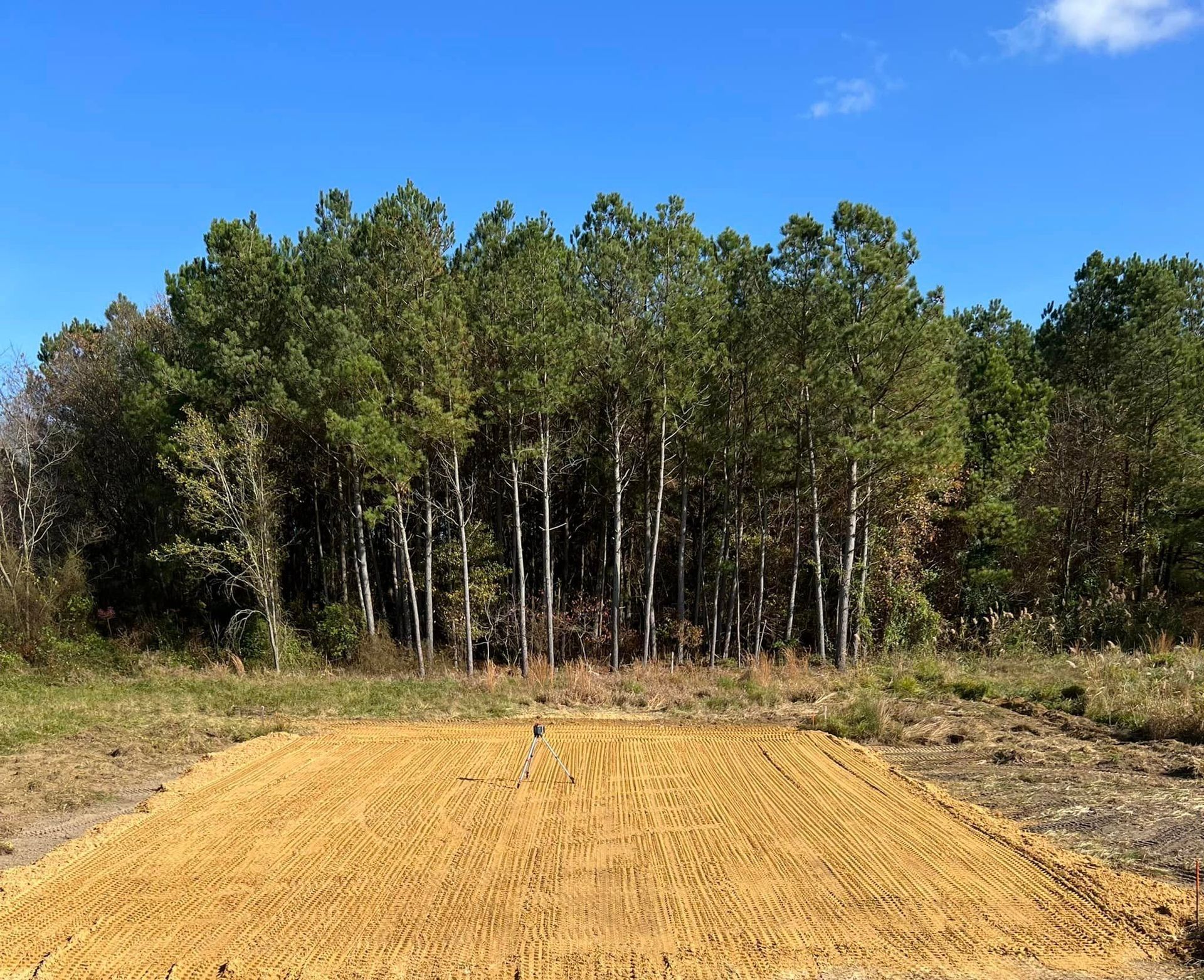 A field of dirt with trees in the background and a blue sky