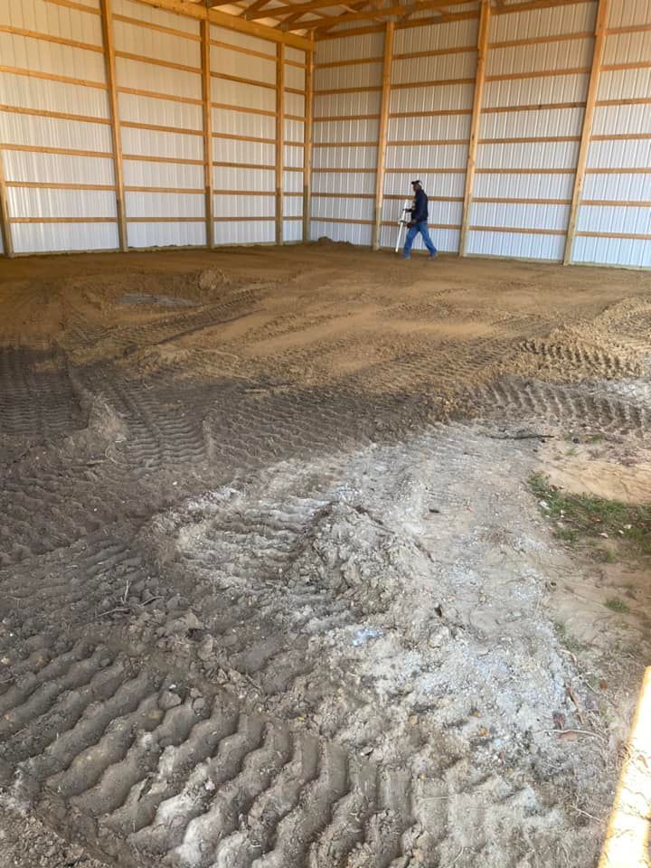 A man is standing in a large barn filled with dirt.