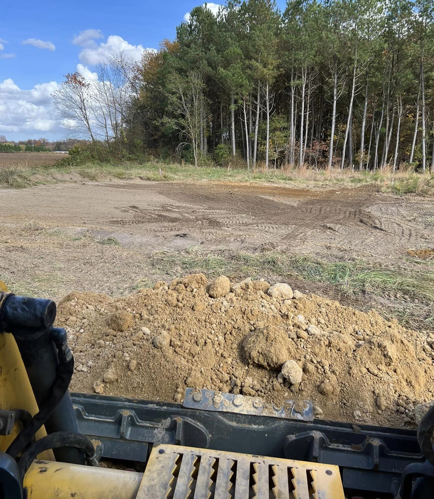 A bulldozer is moving dirt in a field with trees in the background.