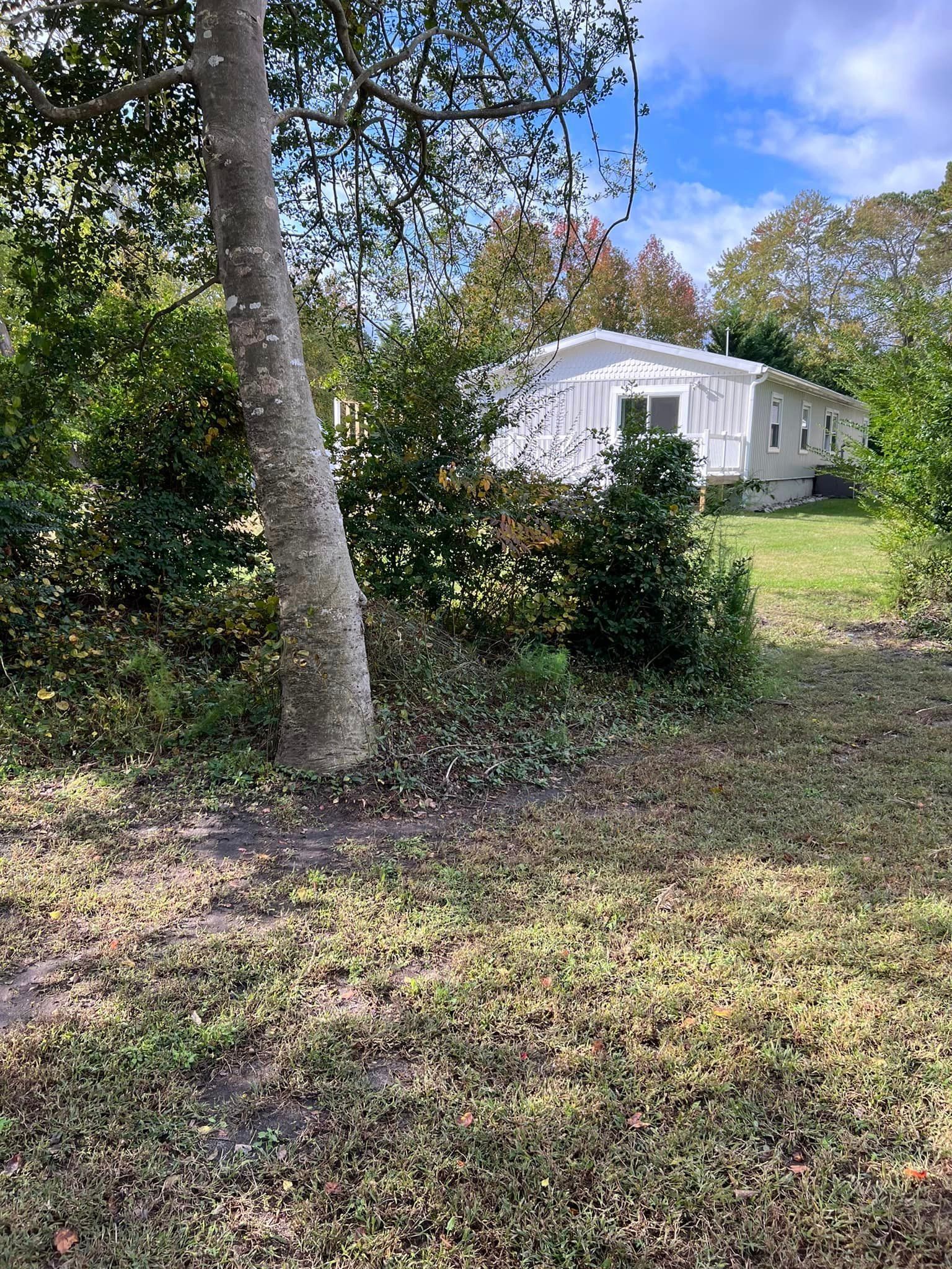 A white mobile home is sitting in the middle of a lush green field surrounded by trees.