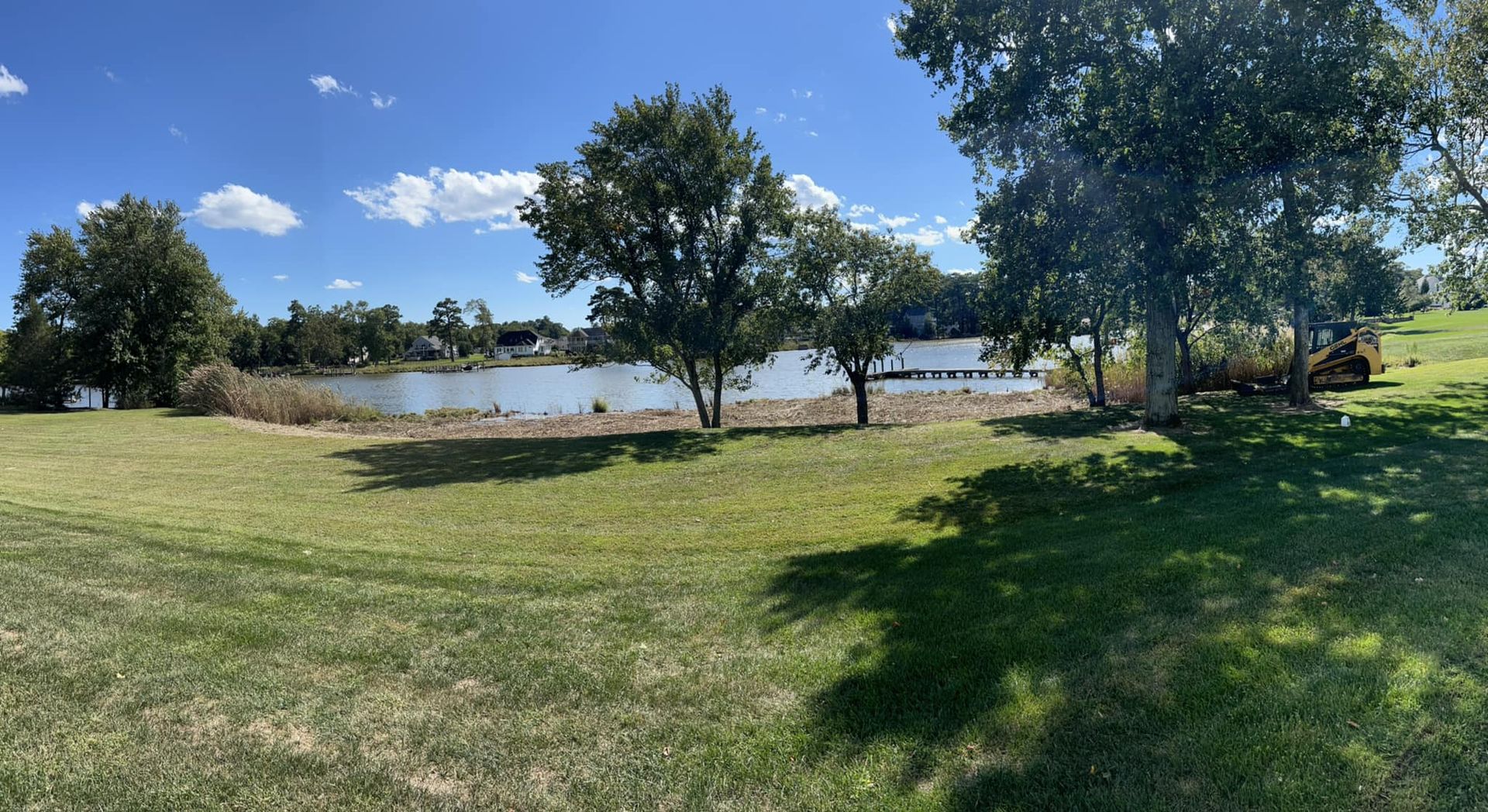 A large grassy field with trees and a lake in the background.