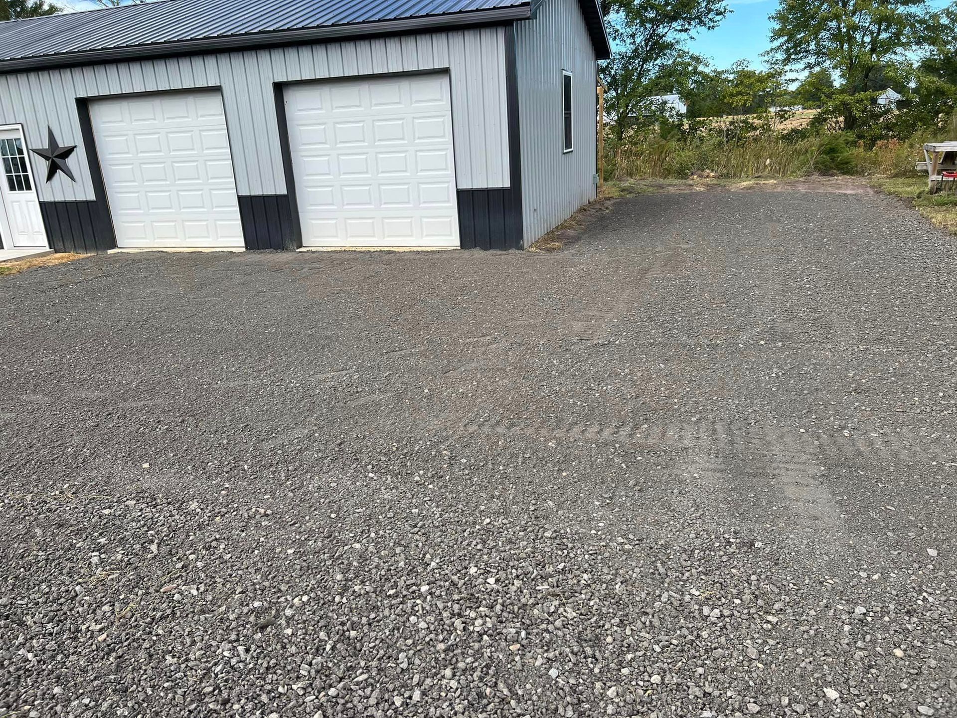A garage with two garage doors and a gravel driveway in front of it.