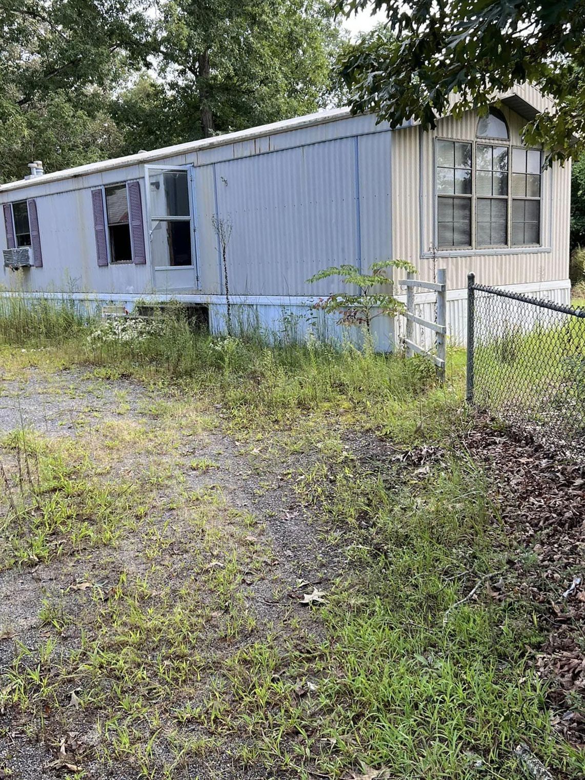 A mobile home is sitting in the middle of a grassy field next to a fence.