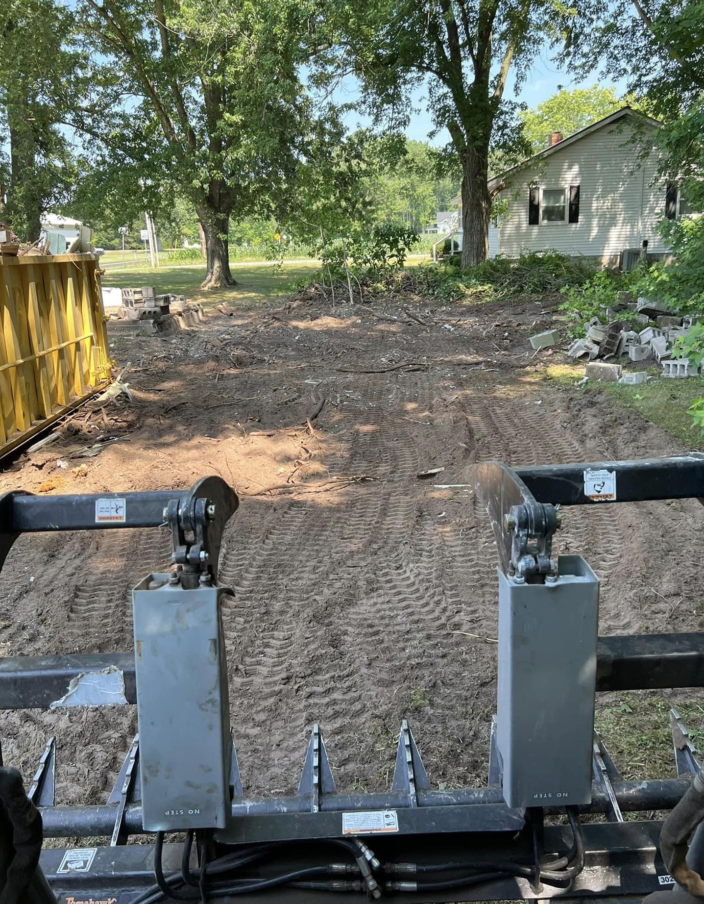 A tractor is driving down a dirt road in front of a house.