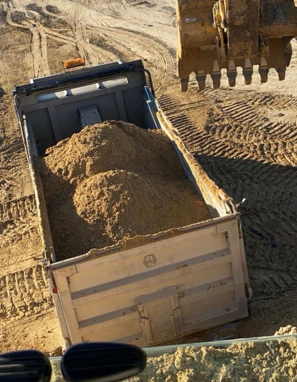 A dump truck filled with sand is being loaded by a bulldozer