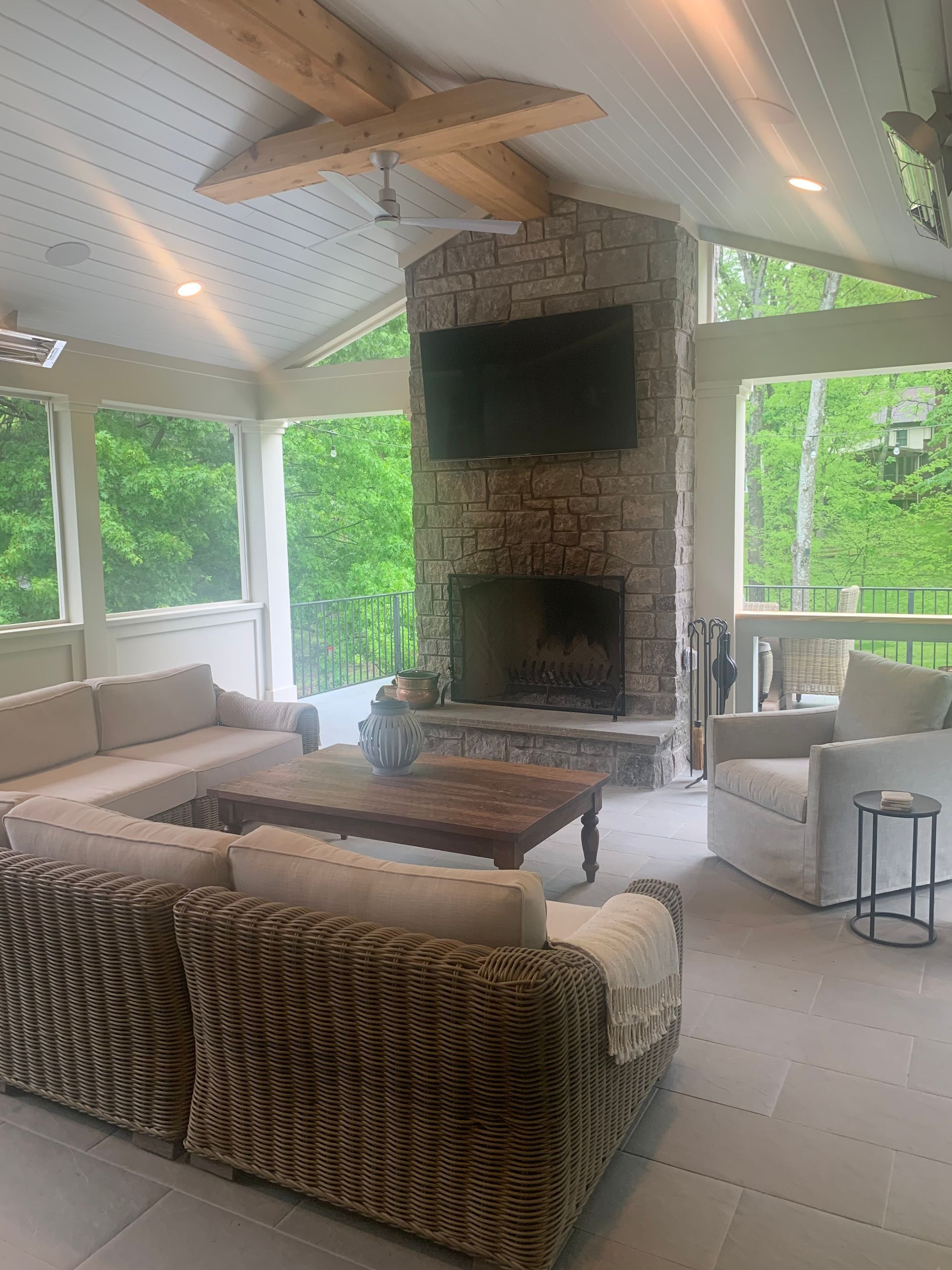 Modern stone patio with a beige sectional sofa, round table, and green cushions against a vine-covered wall.