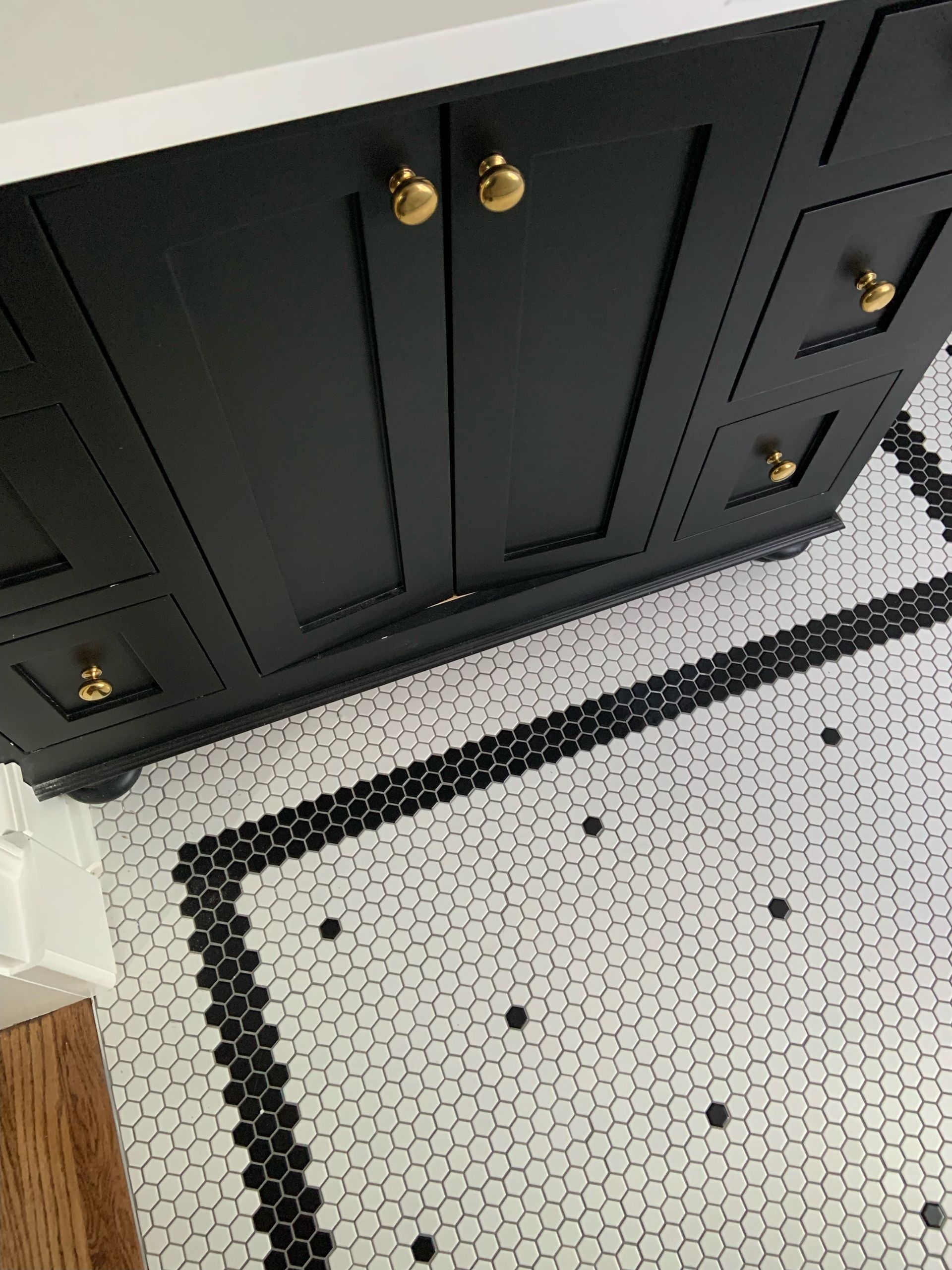 Compact bathroom with gray vanity, toilet, and tiled shower surround in white and black.
