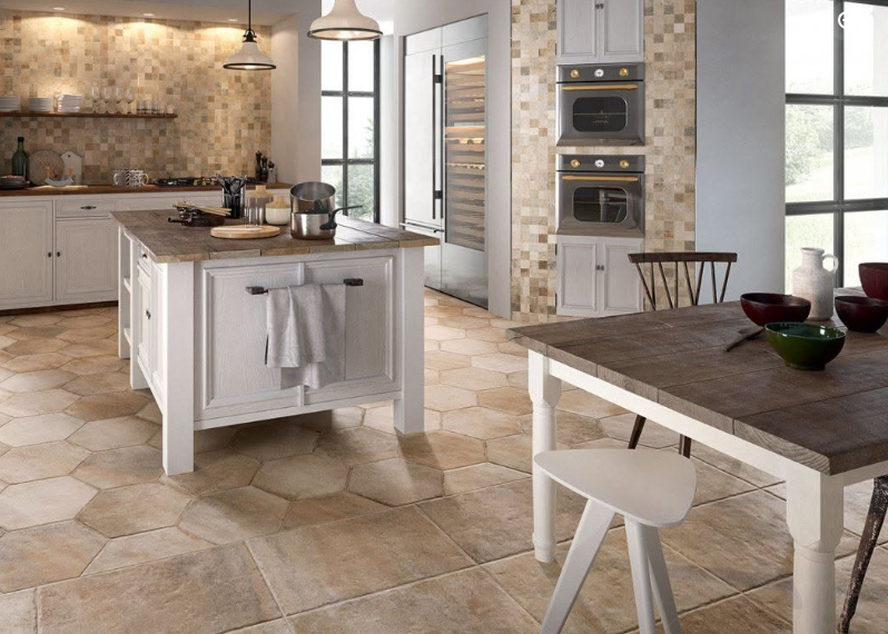 Bright modern kitchen with white island, tiled floor, built-in ovens, and a small dining table ליד window.