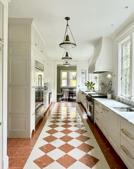 Bright galley kitchen with white cabinets, marble counters, and terracotta-and-white checker floor.