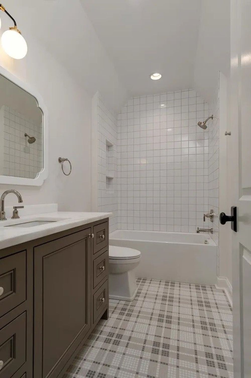 Bright white bathroom with gray vanity, tiled shower-tub, and patterned floor.