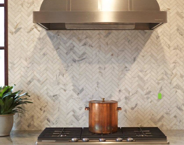 Modern kitchen stovetop with copper pot, stainless hood, and herringbone tile backsplash
