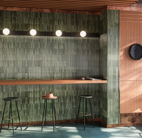Modern bar with green tiled wall, wooden counter, stools, and hanging globe lights in warm daylight