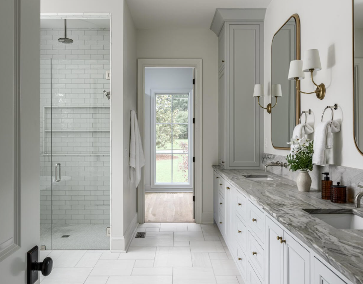 Bright white bathroom with glass shower, long vanity, and a windowed door to greenery