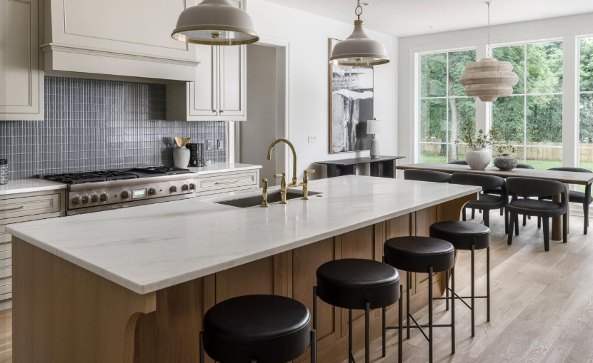 Modern open kitchen with large island, black stools, pendant lights, and dining area by bright windows