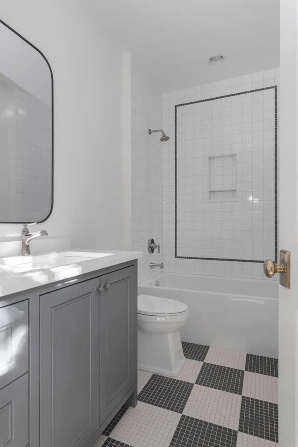 Compact bathroom with gray vanity, toilet, and tiled shower surround in white and black.