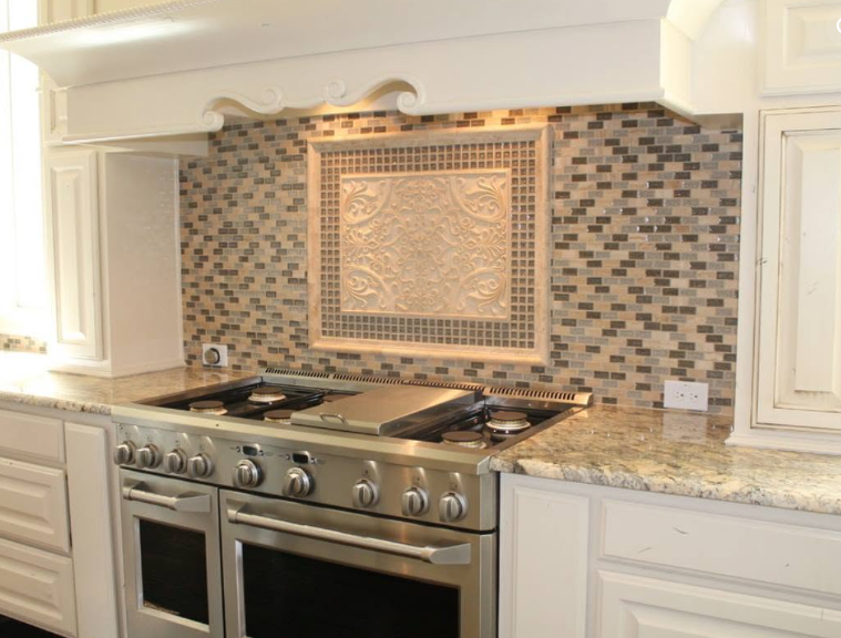 Luxury kitchen backsplash with mosaic tile behind a stainless steel stove and decorative hood