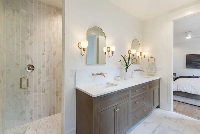 Bright bathroom with glass shower, double vanity, and gold wall sconces