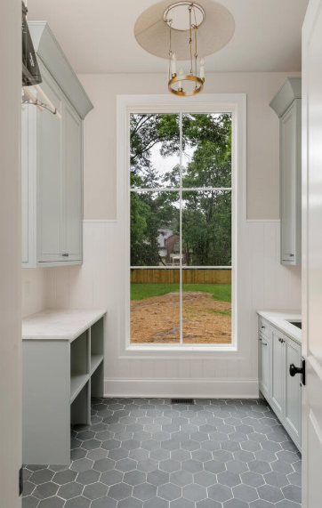 Small bright hallway with gray patterned tile, white built-ins, and a tall window overlooking a yard.