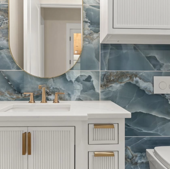 Elegant bathroom vanity with gold fixtures, oval mirror, and blue marble tile backsplash