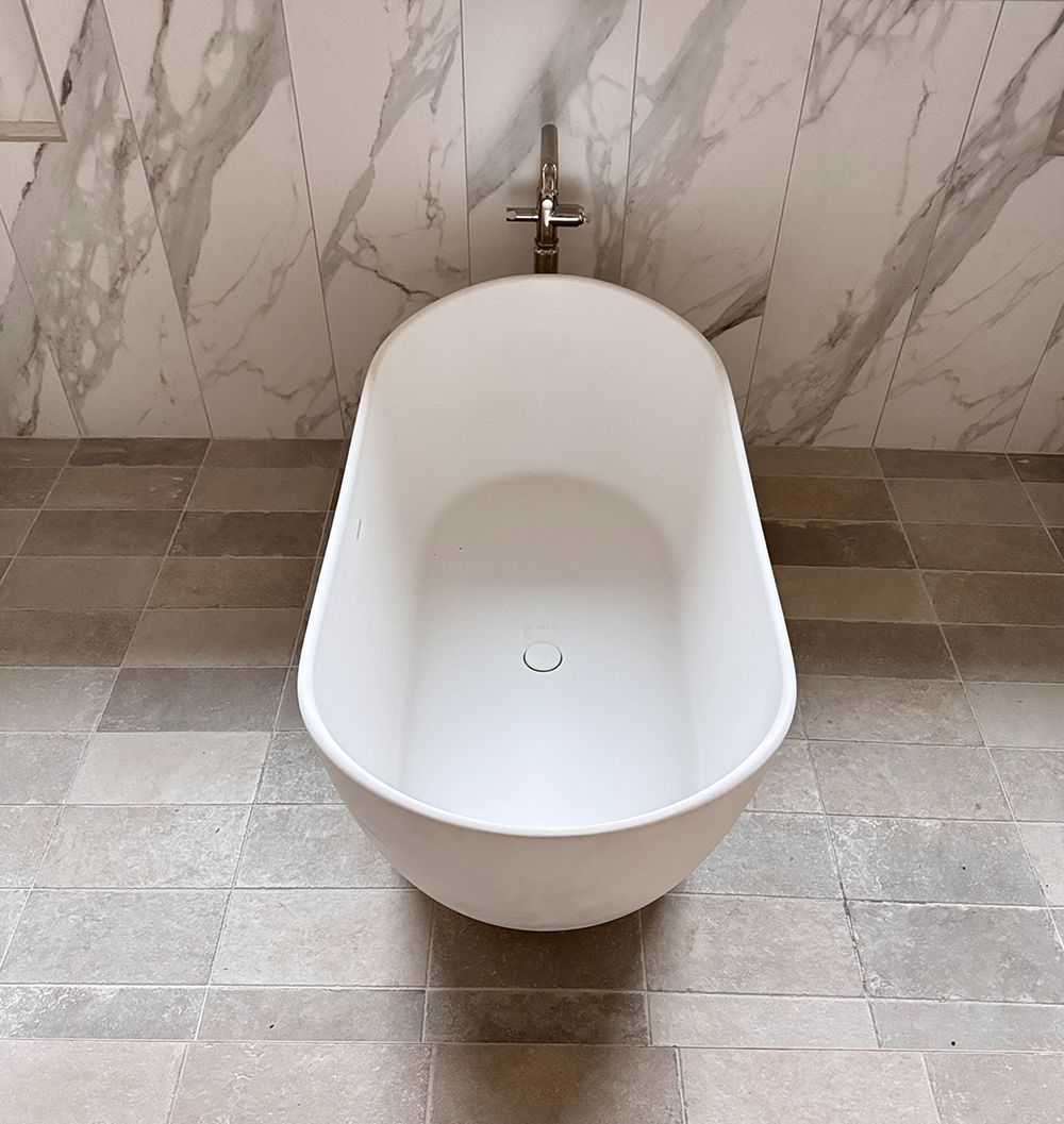 White freestanding bathtub centered against a marble-tiled wall and tiled floor.