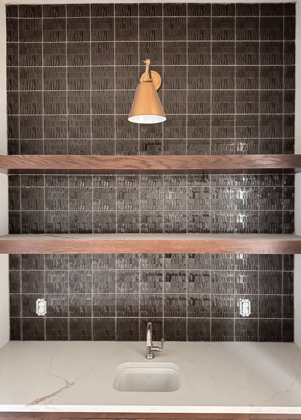 Small kitchen nook with dark tile backsplash, two wooden shelves, sink, and hanging light fixture