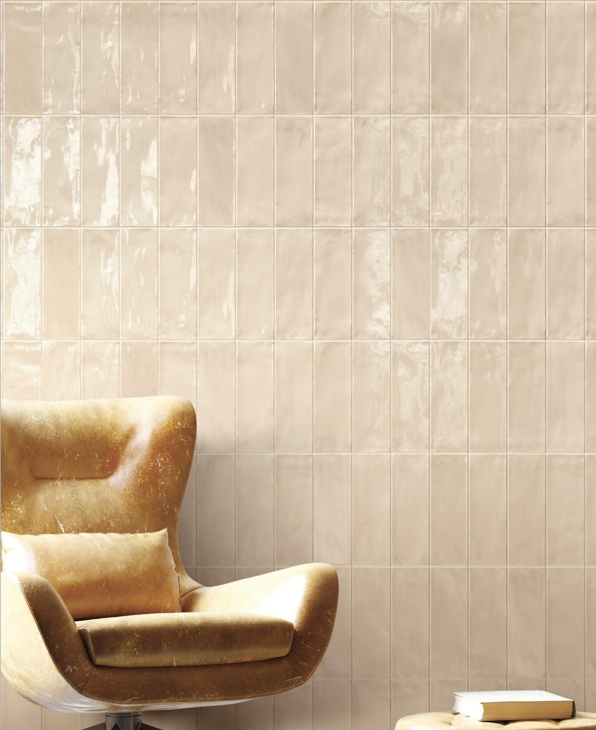 Gold armchair against a cream tiled wall, with a small white side table in the corner.