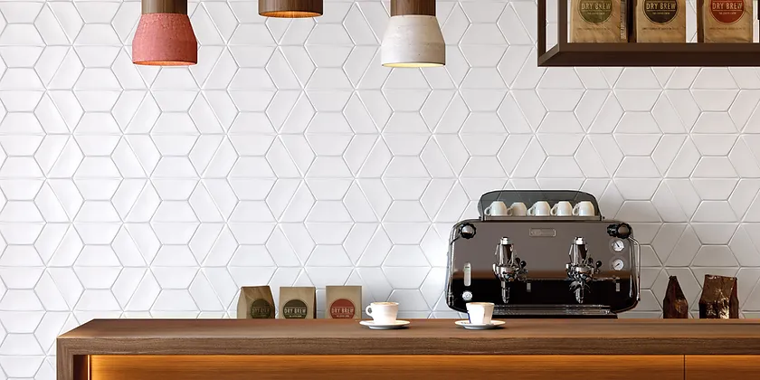Modern café counter with a chrome espresso machine, white hex tile wall, hanging lamps, and wooden shelves