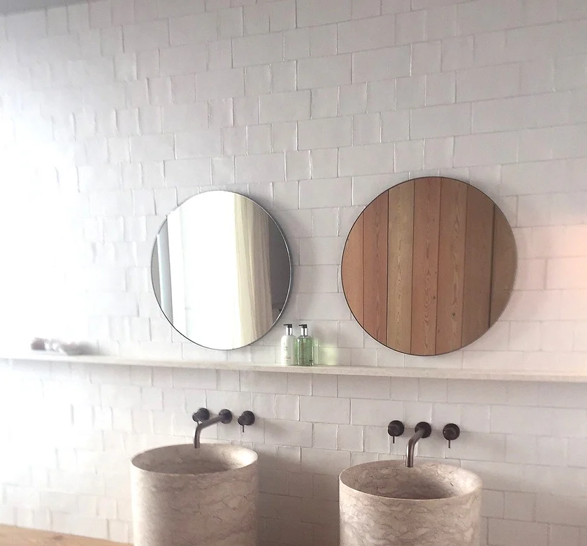 Minimalist bathroom with two round mirrors, stone sinks, and a white tiled wall