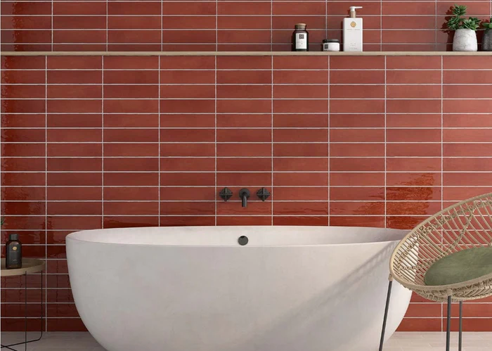 Modern bathroom with red tile wall, white freestanding tub, and woven chair.
