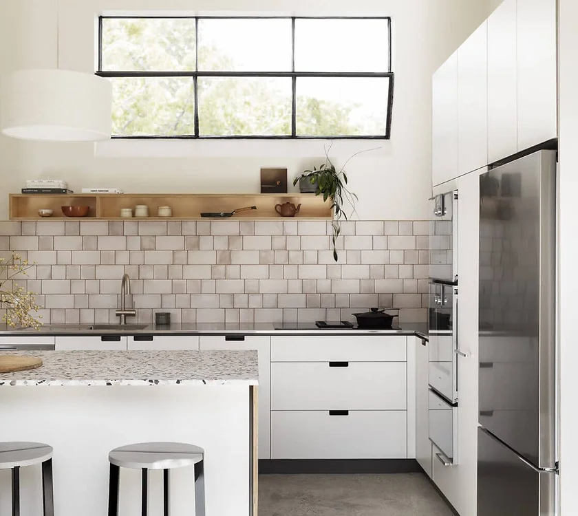 Modern white kitchen with subway tile backsplash, large window, wooden shelves, and stainless-steel refrigerator