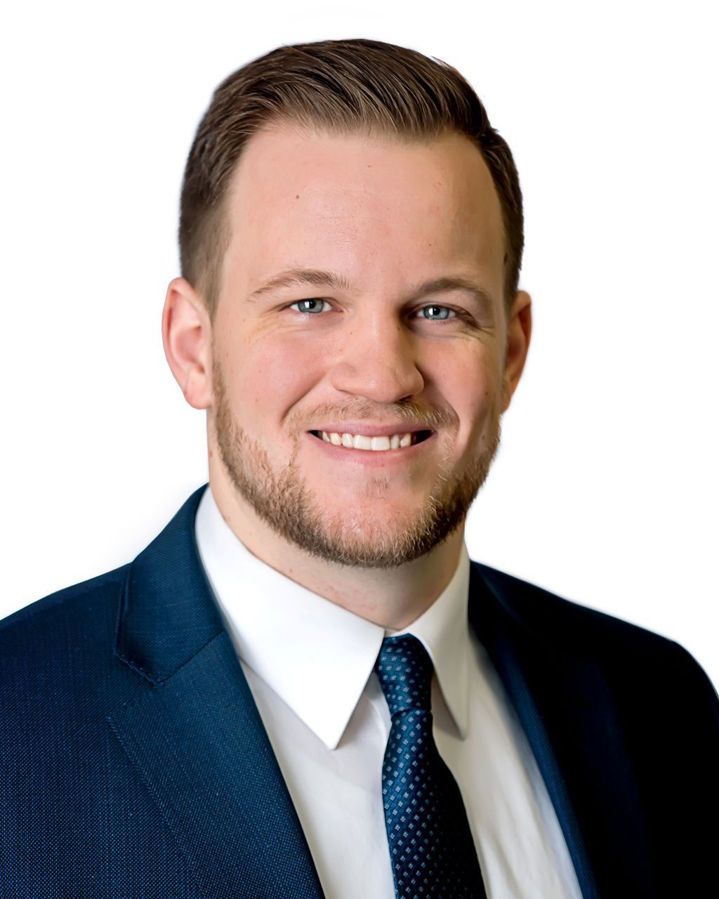Man in a dark blue suit smiling, white shirt, and dark blue tie against a white background.