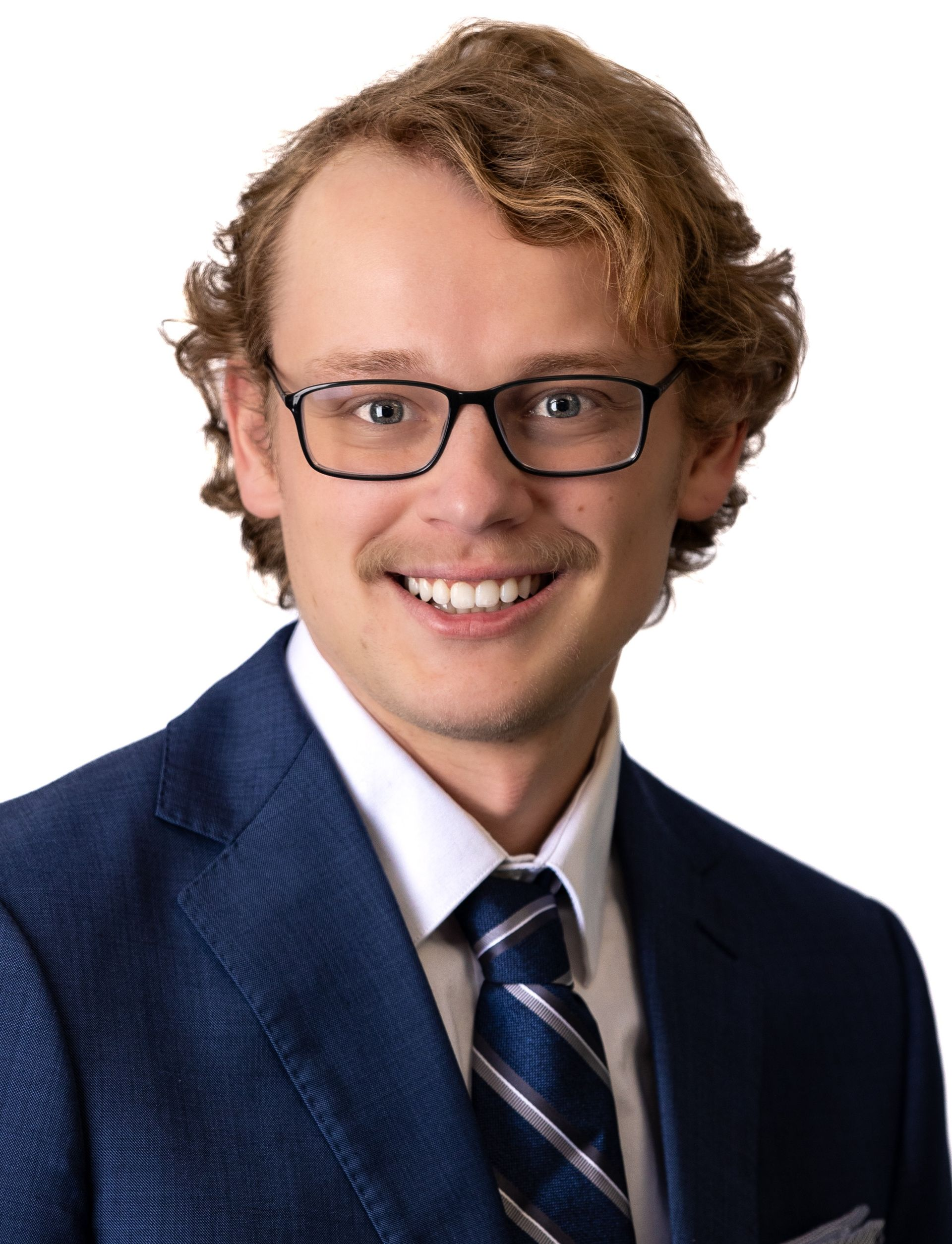 Man in a blue suit and tie, smiling, wearing glasses.