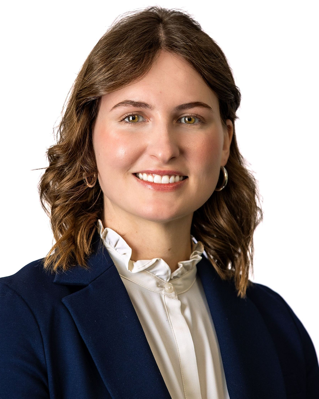 Woman with brown hair smiles, wearing a navy blazer and white blouse, in front of a white background.