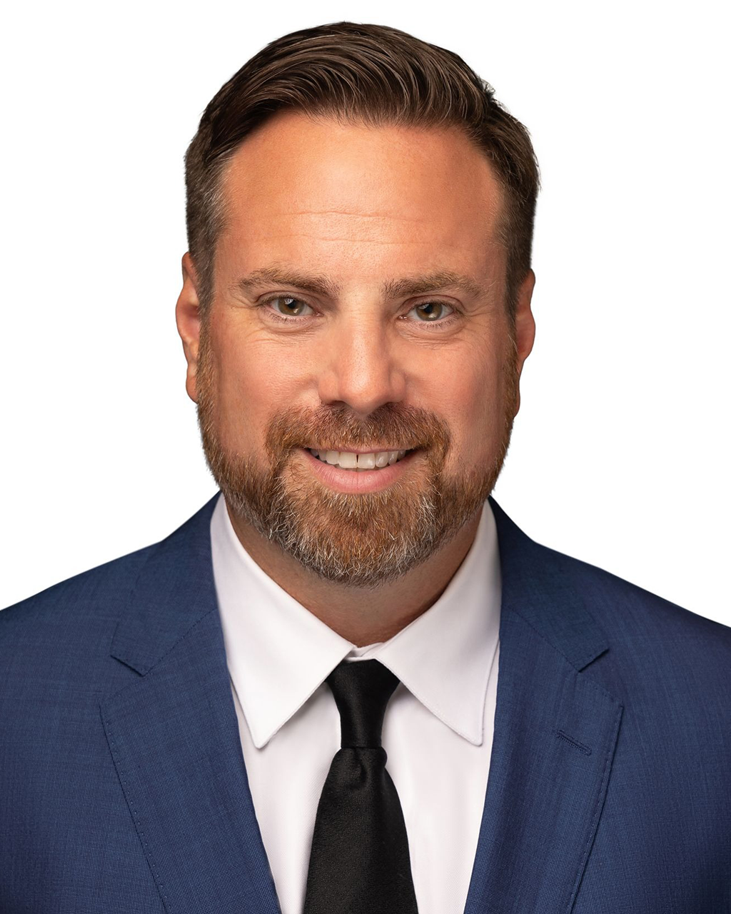 Man in a blue suit smiles, with a trimmed beard and a black tie.