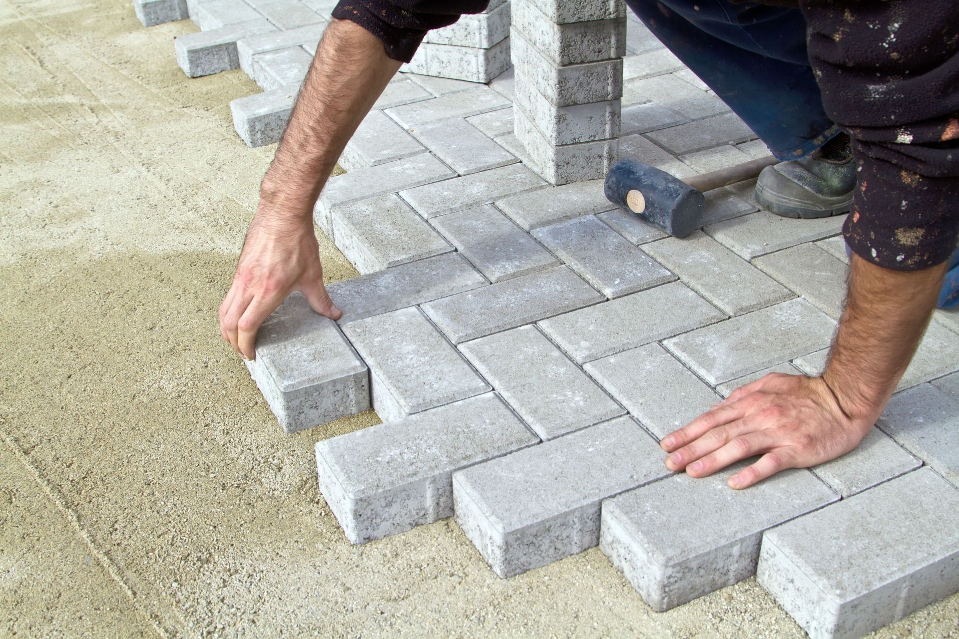 Worker laying gray paving stones by hand on a sandy surface