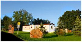 a mobile home illuminated by late afternoon light with a ginat rock resting on the front lawn