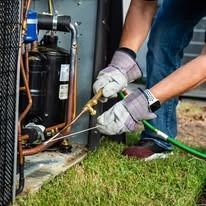A man is working on an air conditioner with a hose.