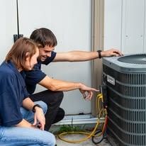 A man and a woman are working on an air conditioner.