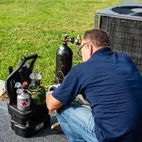A man is kneeling down in front of an air conditioner.
