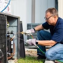 A man is working on an air conditioner outside of a building.