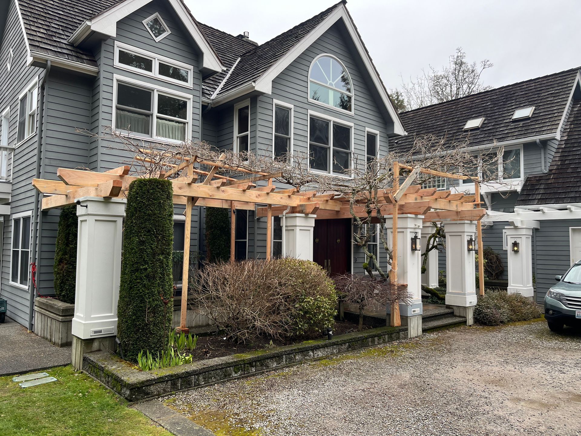 A large gray house with a wooden pergola in front of it.